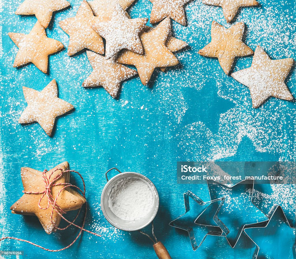 Christmas gingerbread cookies with sugar powder and metal shapes Christmas or New Year holiday food background. Sweet gingerbread cookies in shape of star with sugar powder in sieve and metal shapes on bright blue painted plywood background, top view, copy space Cookie Stock Photo