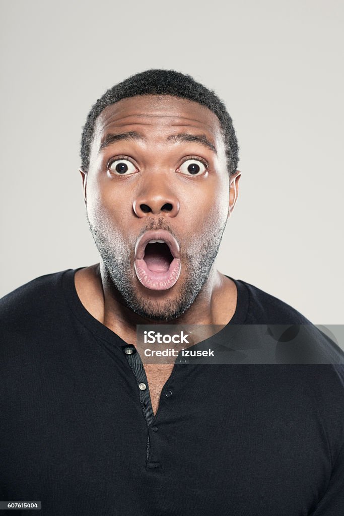 Portrait of surprised afro american young man Portrait of surprised afro american young man wearing black t-shirt, standing against grey background with mouth open, rolling eyes. African-American Ethnicity Stock Photo