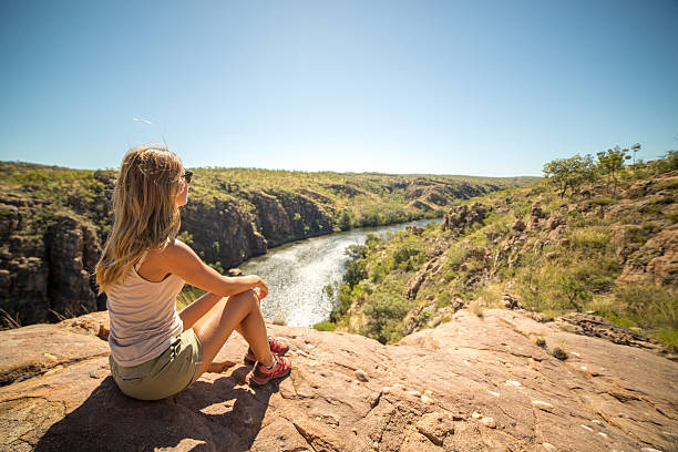une jeune femme qui fait de la randonnée est assise sur la falaise et regarde la vue - emu australia northern territory outback photos et images de collection