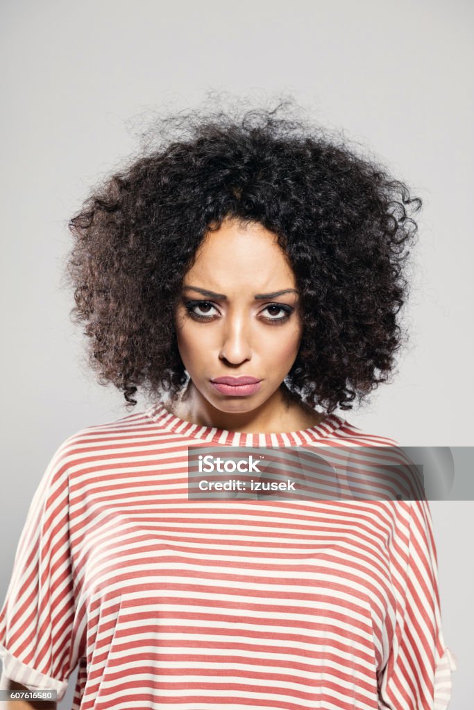 Disappointed afro american woman Portrait of sad afro american young woman wearing striped top, standing against grey background, looking at camera. Adult Stock Photo
