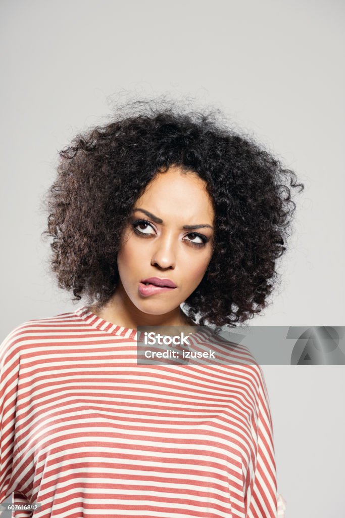 Afro american woman taking a decision Portrait of pensive afro american young woman wearing striped top, standing against grey background, looking up. Contemplation Stock Photo