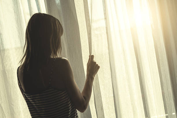 istock Lonesome girl holding a curtain. 607620524