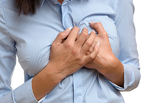 Woman clutching her breast in pain as she suffers the preliminary symptoms of a heart attack or myocardial infarct, close up body view isolated on white