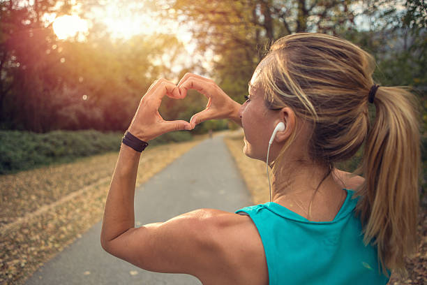 giovane donna sportiva fa la cornice delle dita a forma di cuore al tramonto - jogging autumn young women women foto e immagini stock