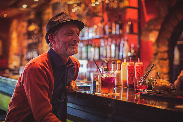 Close-up of a mature trendy man having fun and drinking cocktails in a nightlife cocktail bar. Selective focus. Focus on foreground.