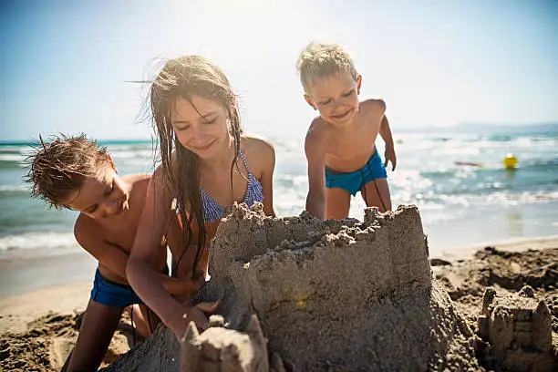 Kids having fun building a sandcastle on the beautiful majorcan beach beach. The girl is aged 10 and the boys are aged 6. Sunny summer day.