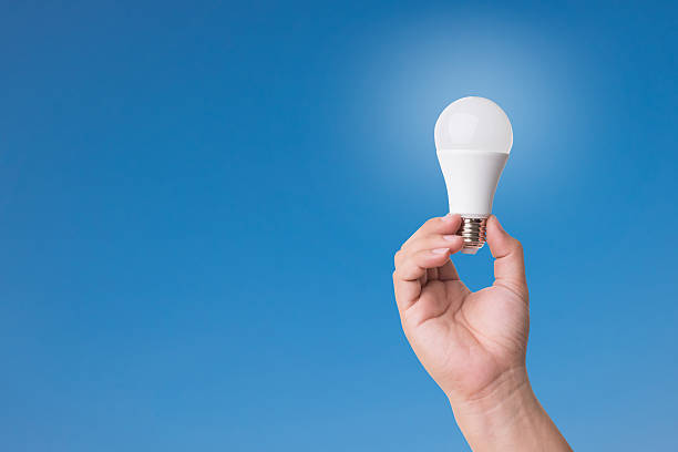 lampadina led con mano con illuminazione su sfondo cielo blu. - led lighting equipment light bulb installing foto e immagini stock