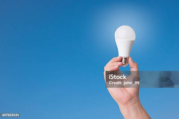 Hand Holding Led Bulb With Lighting On Blue Sky Background Stock Photo - Download Image Now