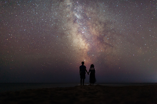 Young Caucasian couple walking near the sea  at night under the starry sky