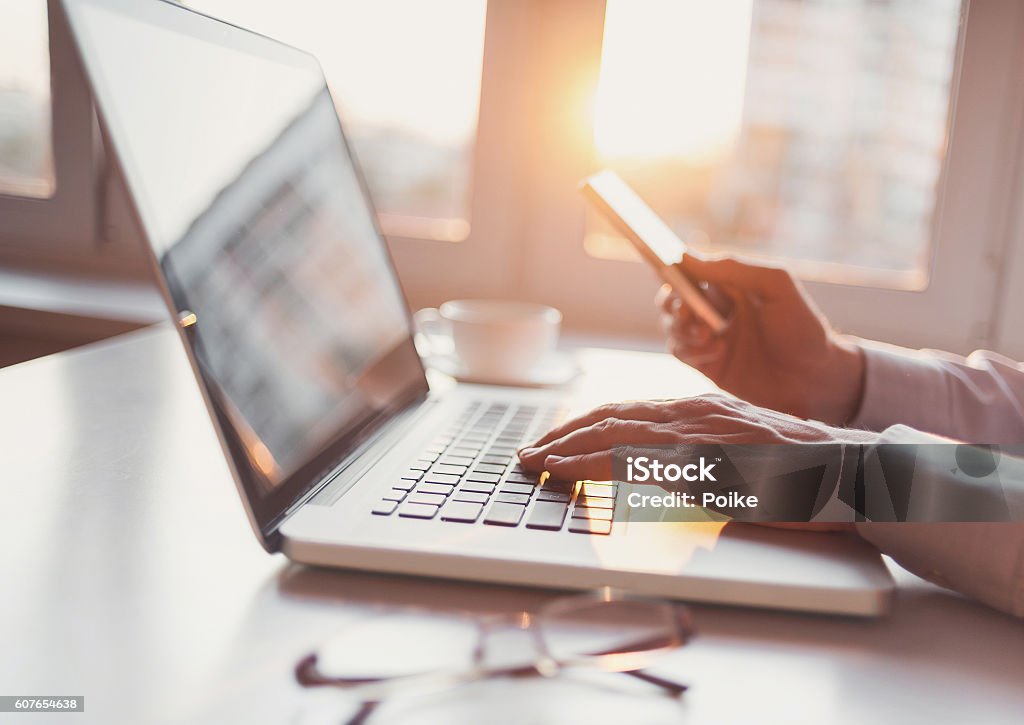 Lugar de trabajo, hombre usando computadora portátil y teléfono inteligente - Foto de stock de Periodismo libre de derechos