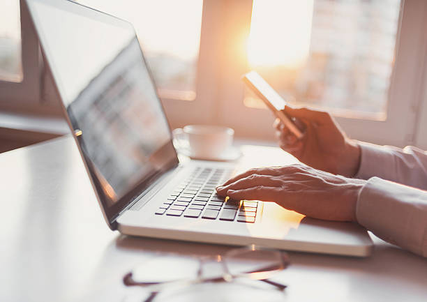 luogo di lavoro, uomo che usa computer portatile e smartphone - telephone dialing human hand office foto e immagini stock