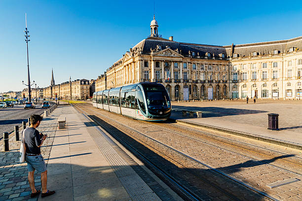 Bordeaux, France - July 19, 2016: Young male bordelais on his mobile waiting for the tram during the morning commute at Place de la Bourse, Bordeaux. The tram and cycle networks throughout the city centre contribute to a more relaxed atmosphere than most other big cities.