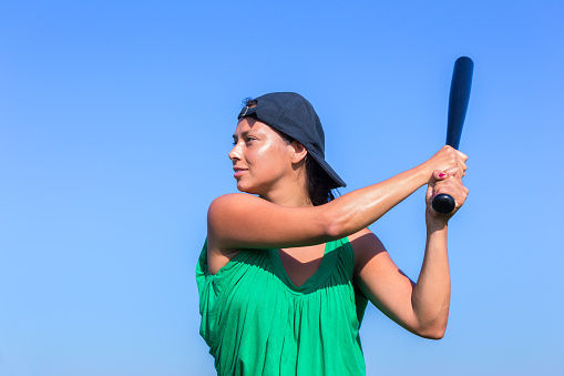 Young european woman with baseball bat and cap in blue sky. The dutch woman looks rather sturdy and tough on this photo. I took the image on a sunny day in summer to get a background with blue sky. Concept of active,activity,sport,sports,baseball,bat,cap,long hair,summer,summertime,ready,hit,play,game, sport, sportswoman, athlete, sport woman, sports, sporty, sporting.