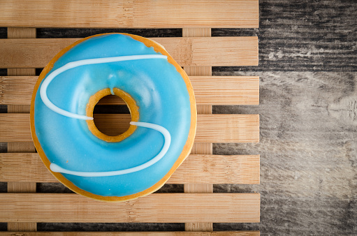 Vintage photo of a sweet iced donut on wooden background, served on a bamboo plate. Hardwood oak table. Studio shot. Soft post processing.