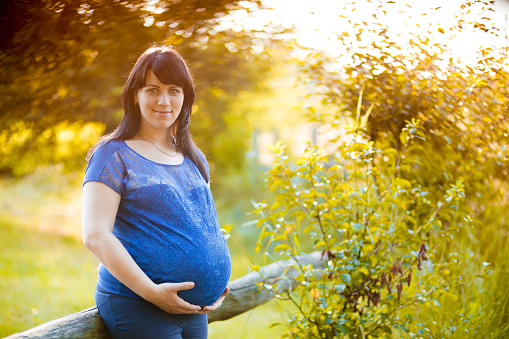 Pregnant woman posing in a green garden summer