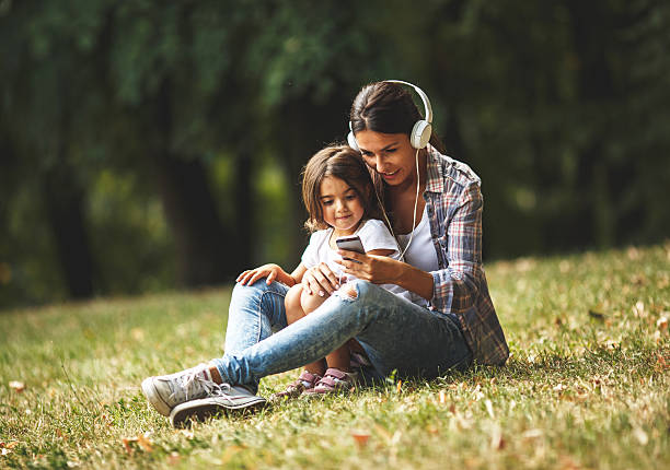 mother sitting with her daughter and using smartphone - parent mother music listening imagens e fotografias de stock