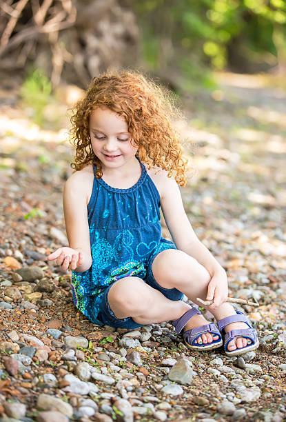Girl Playing On Bank Of Mississippi River Young girl with curly red hair sitting on the bank of the Mississippi River on a summer day in Minnesota, USA. She is looking down at the rocks she has just picked up with her right hand. riverbank photos stock pictures, royalty-free photos & images