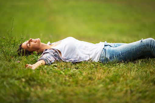 Young woman lying down on grass.She enjoys in the moment of peace.