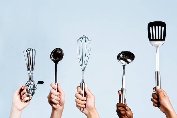 Five mixed hands hold up a kitchen ladle, a spoon, a beater, a whisk, and an egg lifter. They're ready to cook almost anything!