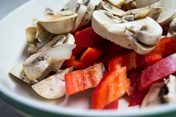Some freshly sliced mushrooms and red bell peppers, ready to be used in cooking, such as on a pizza or in a sauce.