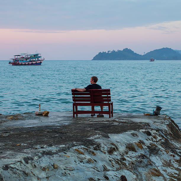 istock Man sits alone on a stone cliff of  sea coast 607753614