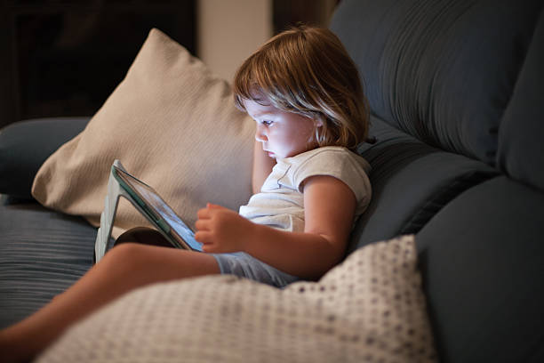 little child sitting comfortably in sofa watching tablet - fotografia de stock