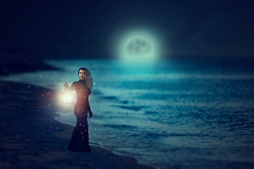 attractive and misterious woman in fairy shot holding lantern and looking away.photo taken in the night on the beach.