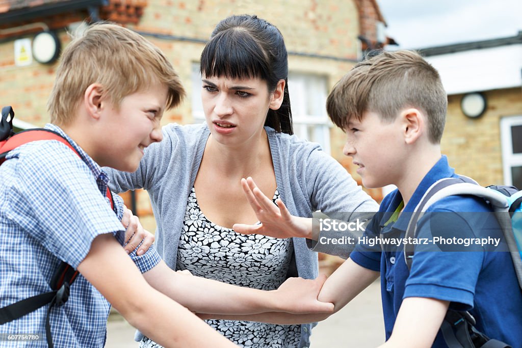 Teacher Stopping Two Boys Fighting In Playground Education Stock Photo