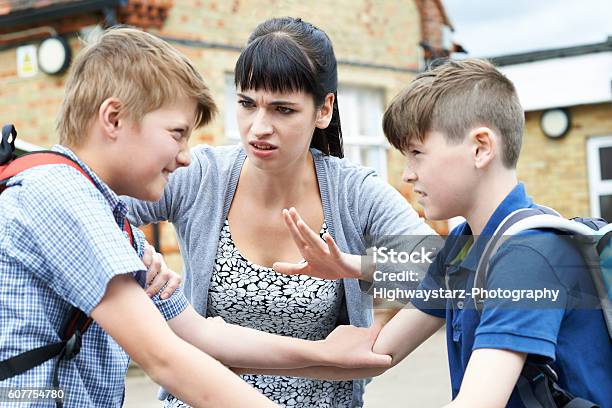 Teacher Stopping Two Boys Fighting In Playground Stock Photo - Download Image Now - Education, Conflict, Arguing