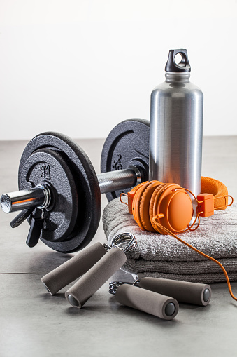 sport, healthy lifestyle and equipment concept - still-life of dumbbells, hand grip with orange earphones and aluminum flask