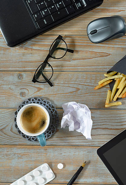 bureau en désordre avec déjeuner, ordinateur, lunettes et paracétamol pour le stress - overstrained photos et images de collection