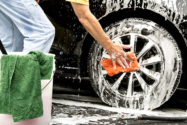 istock Man cleaning soapy car tire and wheel with sponge 607761636