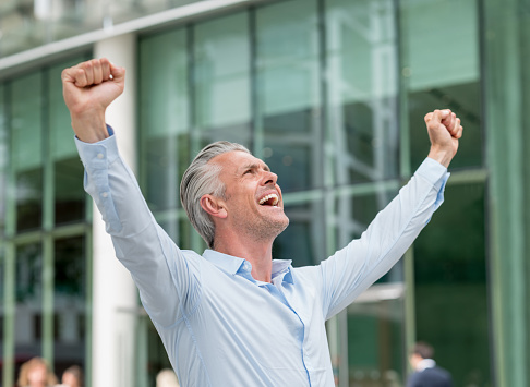 Successful business man celebrating his triumph with arms up and looking very happy