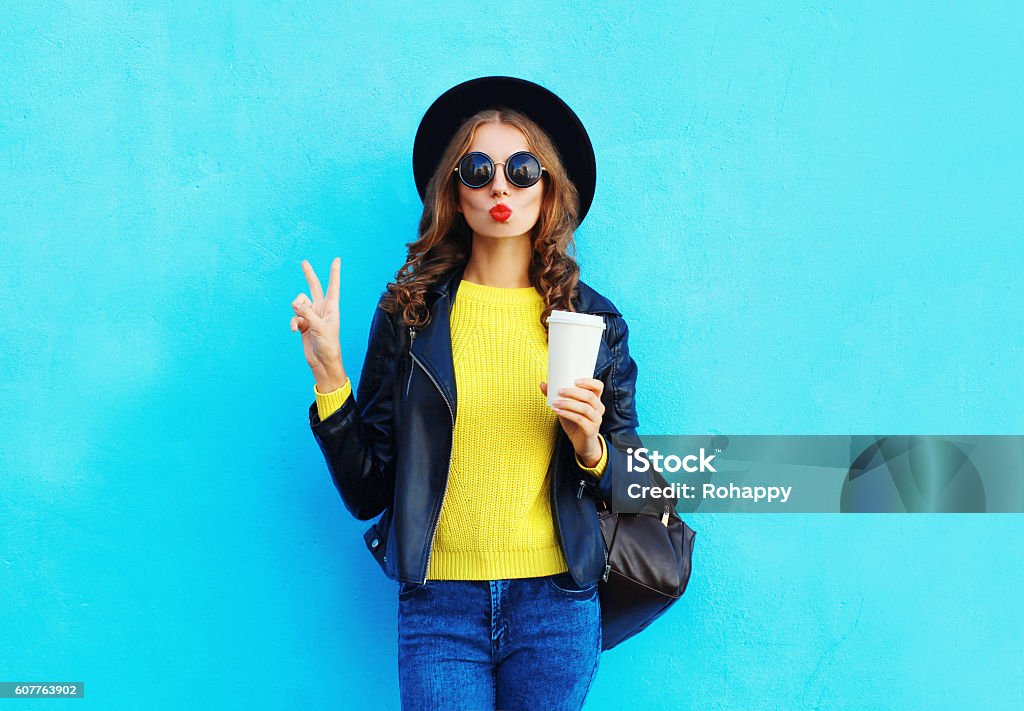 Fashion pretty woman with coffee cup wearing black rock style Fashion pretty woman with coffee cup wearing black rock style clothes over colorful blue background Teenage Girls Stock Photo