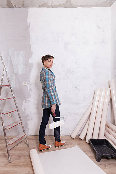 istock Pretty woman with roller paste wallpaper repair house 607767466