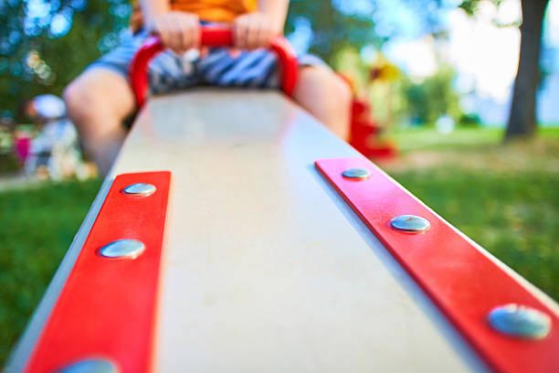 Boys playing on a seesaw on a playground in a sunny day