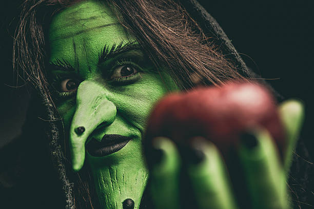 evil witch looking at camera holding a red apple - rudeness ugliness clothing people imagens e fotografias de stock