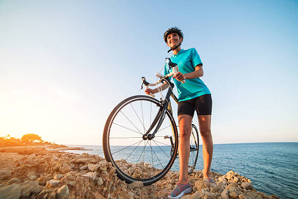 istock Female cyclist standing on a rock and looking at sea 607774624