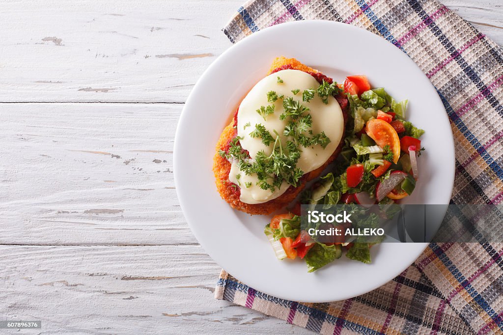 Italian chicken Parmigiana and salad. horizontal top view Italian chicken Parmigiana and fresh vegetable salad on a plate on the table. horizontal top view Parmesan Cheese Stock Photo