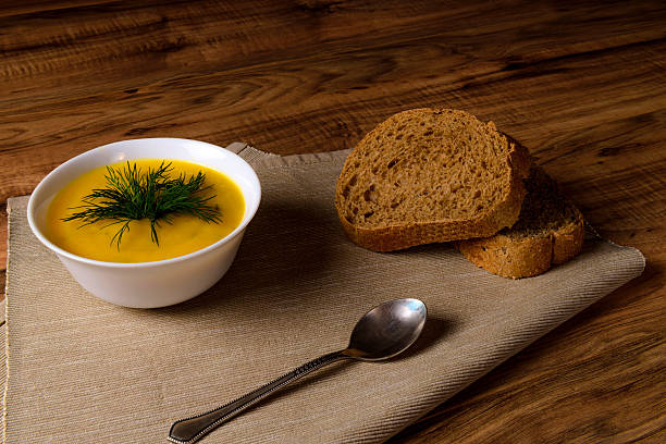 Bowl of pumpkin soup with bread and greens on a wooden surface