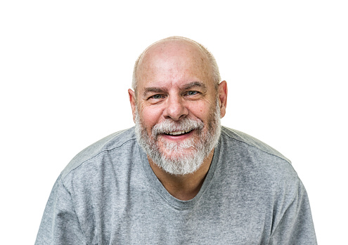 A 60-something senior adult man is smiling as he looks at the camera with a friendly facial expression. He is balding, with short hair and a full grey beard and mustache. He is casually dressed in a grey t-shirt.