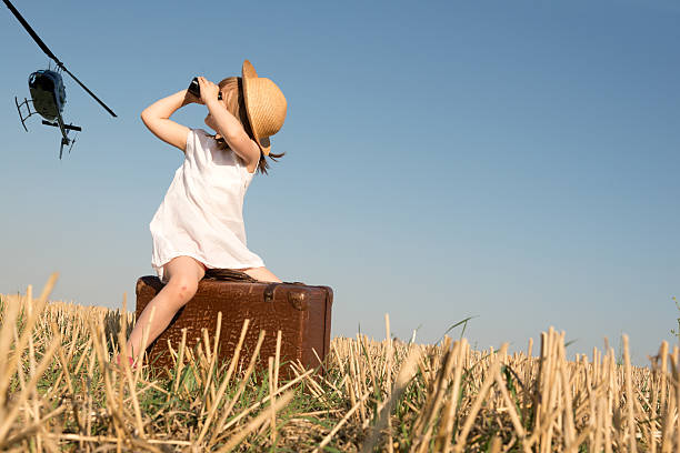 Holiday background – Little girl with binoculars and suitcase is waiting for helicopter