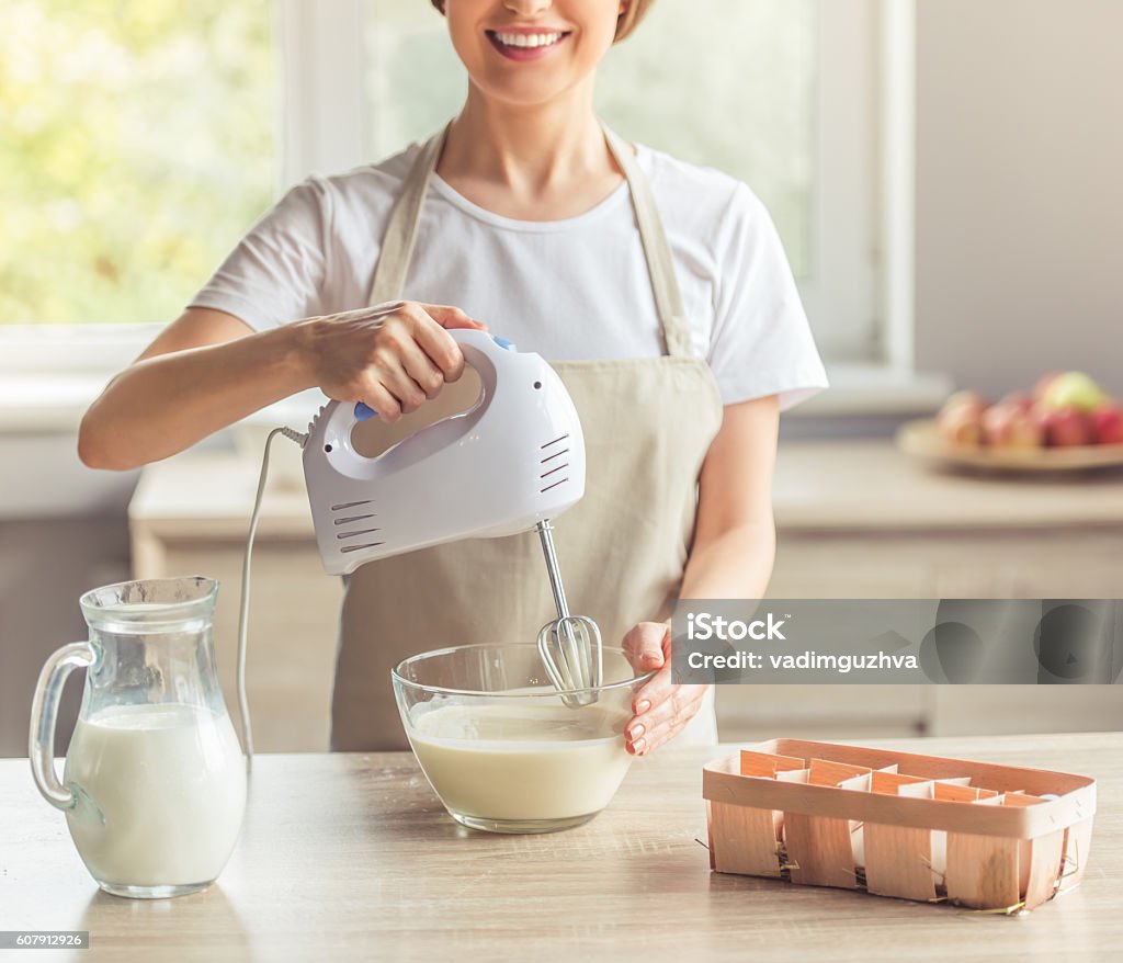 Beautiful woman baking Cropped image of beautiful woman in apron smiling while mixing liquid dough for baking using an electric mixer Electric Mixer Stock Photo