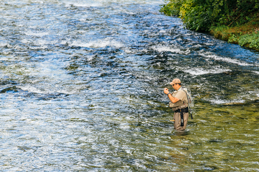 Ribcev Laz, Slovenia - August 22, 2016: Unidentifiable man fishing at Jezernica, second shortest river in Slovenia, flowing from Lake Bohinj for 100 meters to join Mostnica and form Sava Bohinjka.