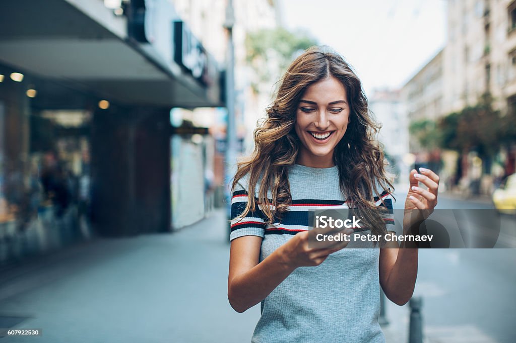 Attractive young woman texting on the street Smiling young woman with smart phone walking on the street, with copy space. Mobile Phone Stock Photo