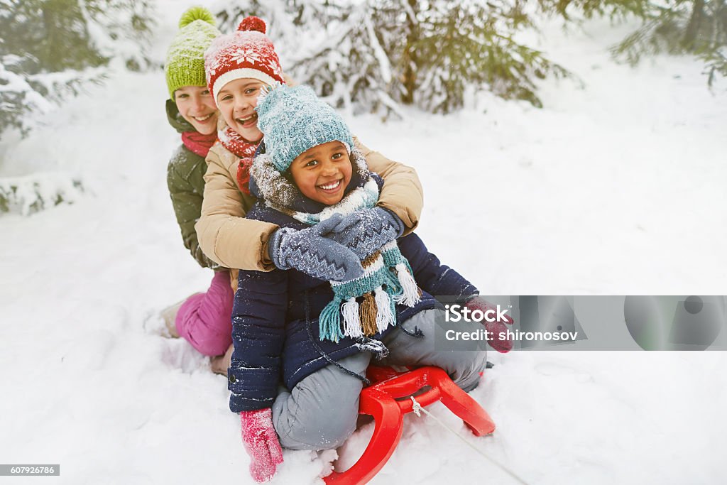 Adorable girls Three multi-ethnic girls on sledge having fun in snow Child Stock Photo