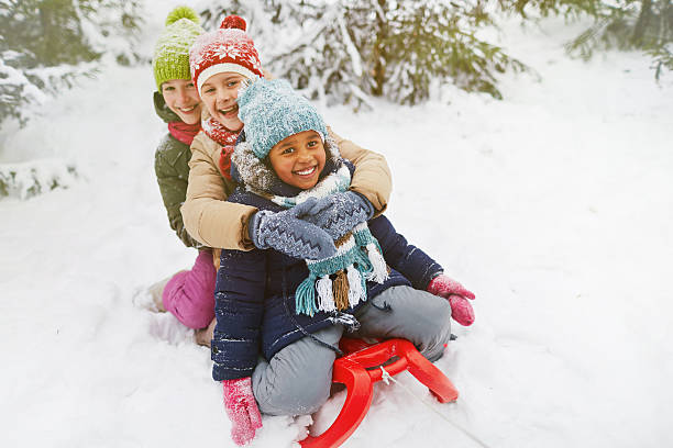 Adorable girls Three multi-ethnic girls on sledge having fun in snow children in winter stock pictures, royalty-free photos & images