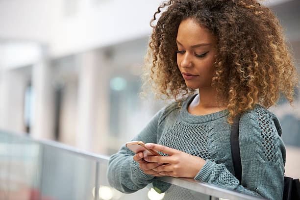 istock Smiling mixed race young woman uses phone in modern interior 607927540
