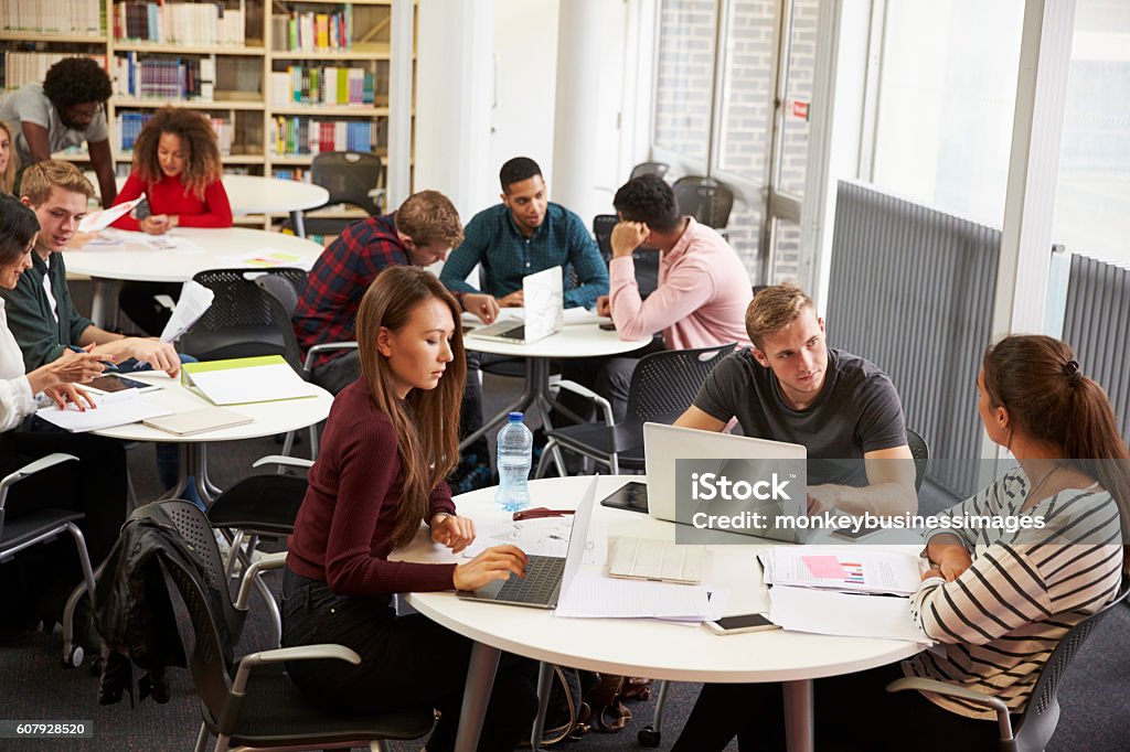 Busy University Library With Students And Tutor Teacher Stock Photo