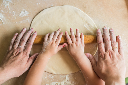 Children and dad hands rolled dough with a rolling pin on the table